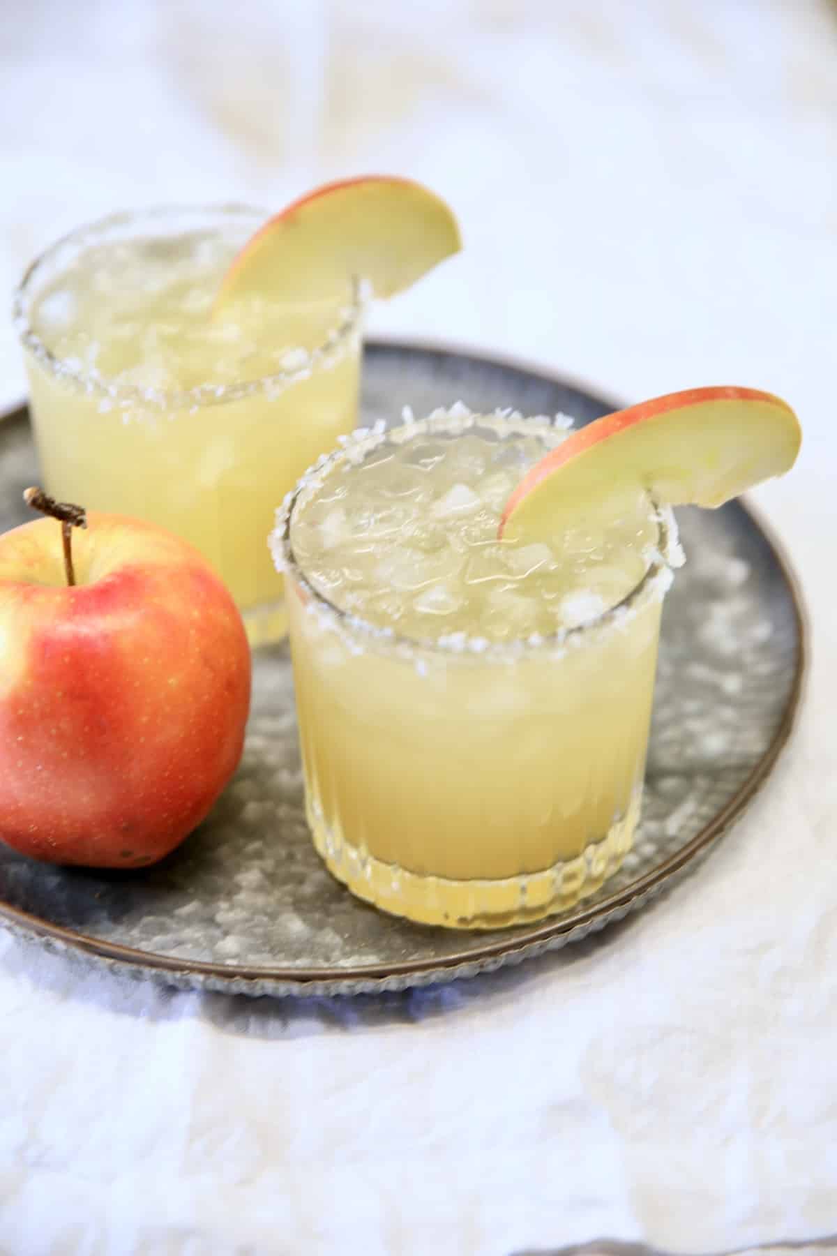 2 margaritas on a tray with apple garnish.