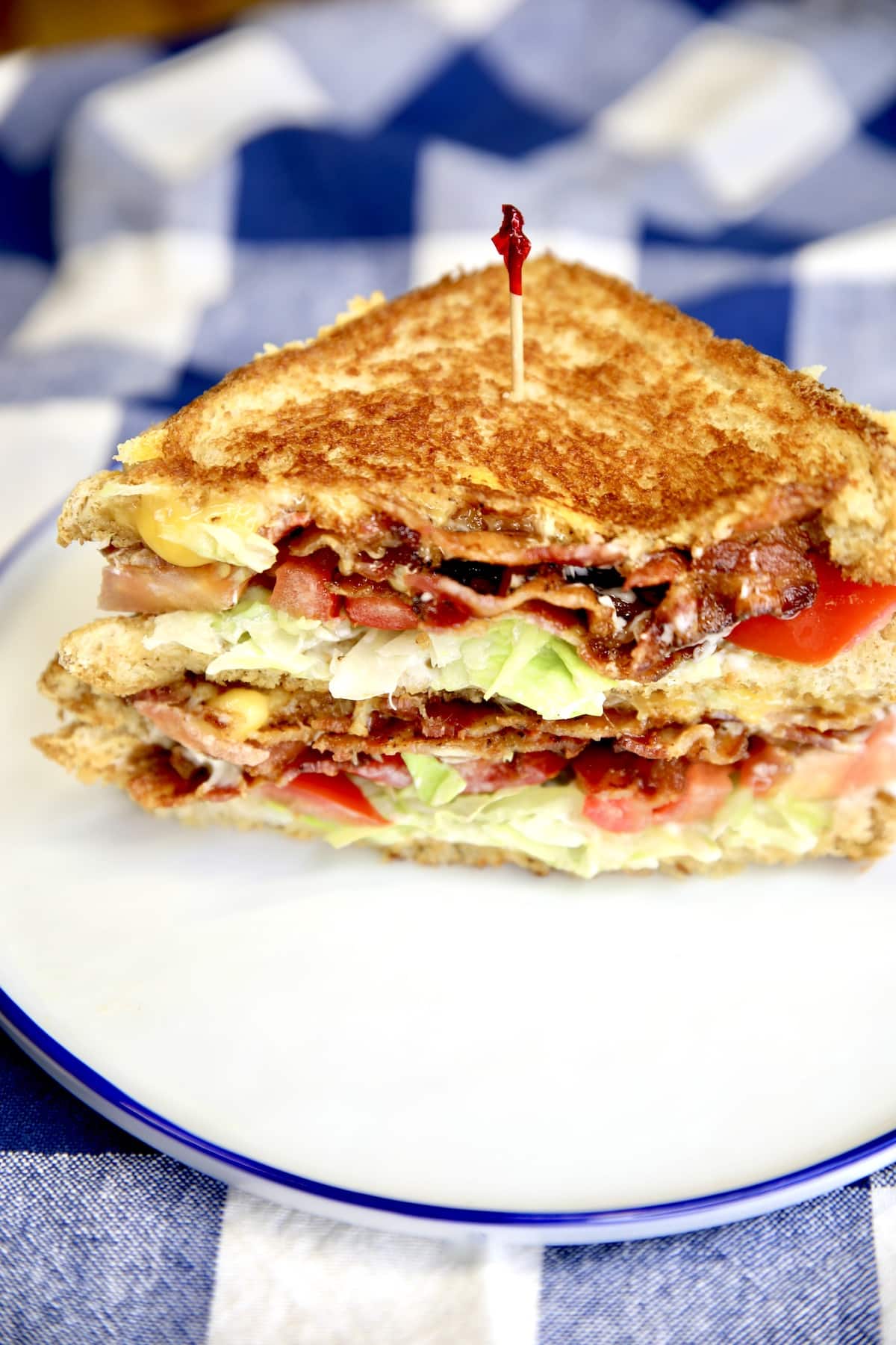 BLT Grilled Cheese, cut in half on a plate, stacked.