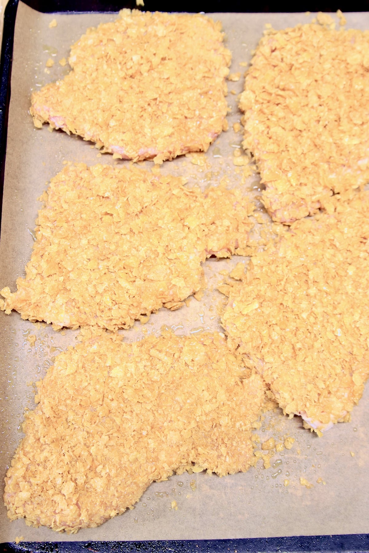 Pork chops breaded with cornflakes on a baking sheet.
