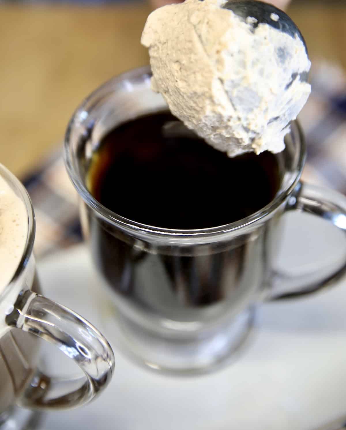 Adding a scoop of whipped cream to mug of coffee.