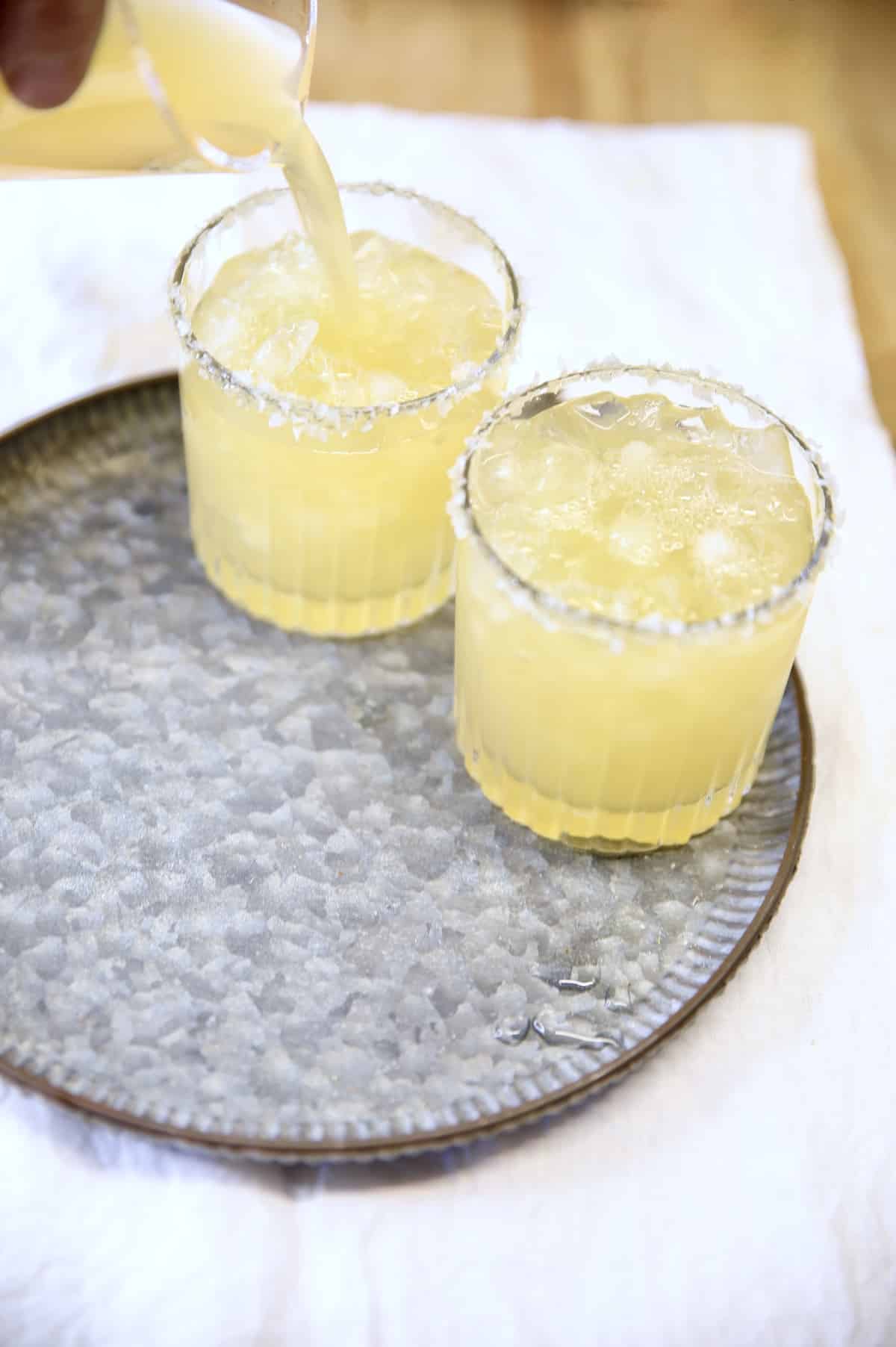 Filling cocktail glasses with apple cider margaritas on a platter.