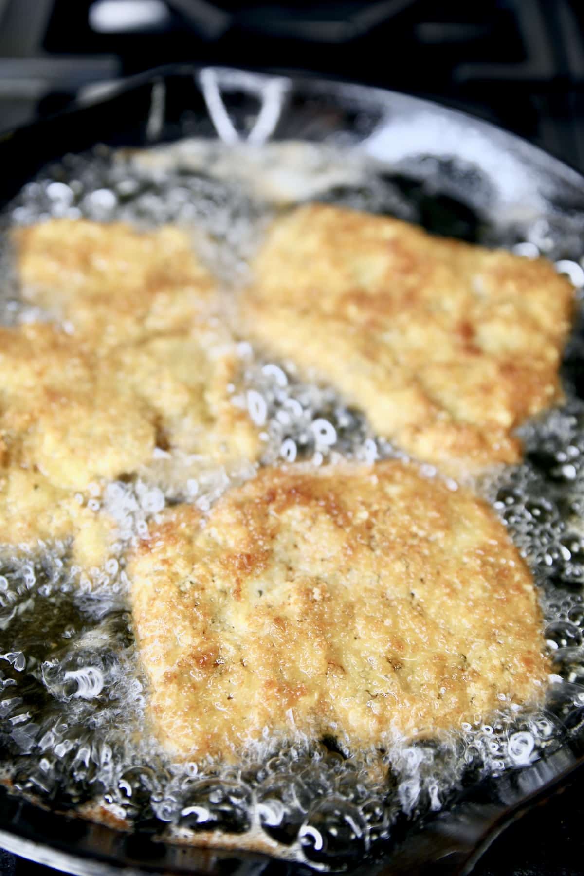 Frying chicken parmesan in a skillet.