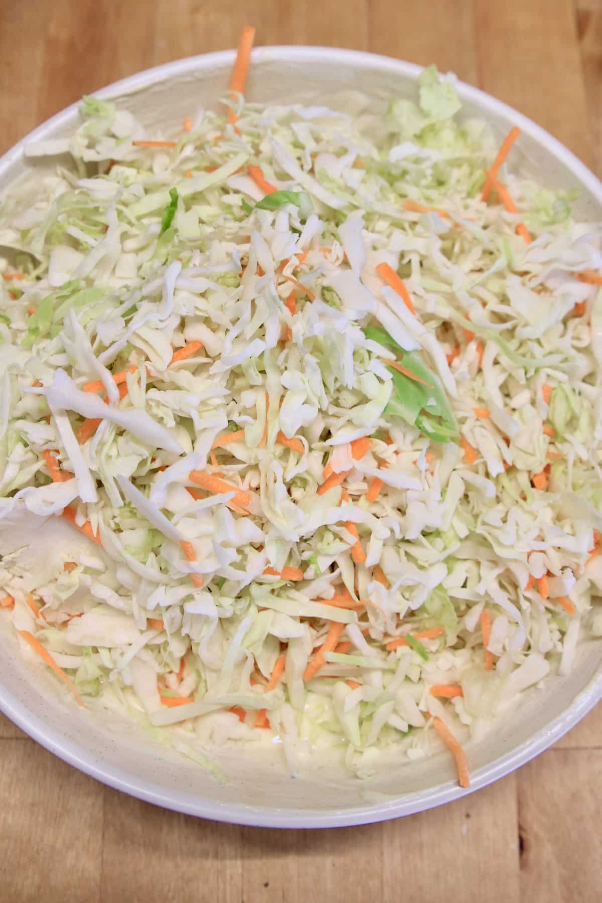 Shredded cabbage and carrots in a bowl with slaw dressing.