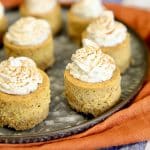Mini pumpkin cheesecakes with whipped cream on a platter.