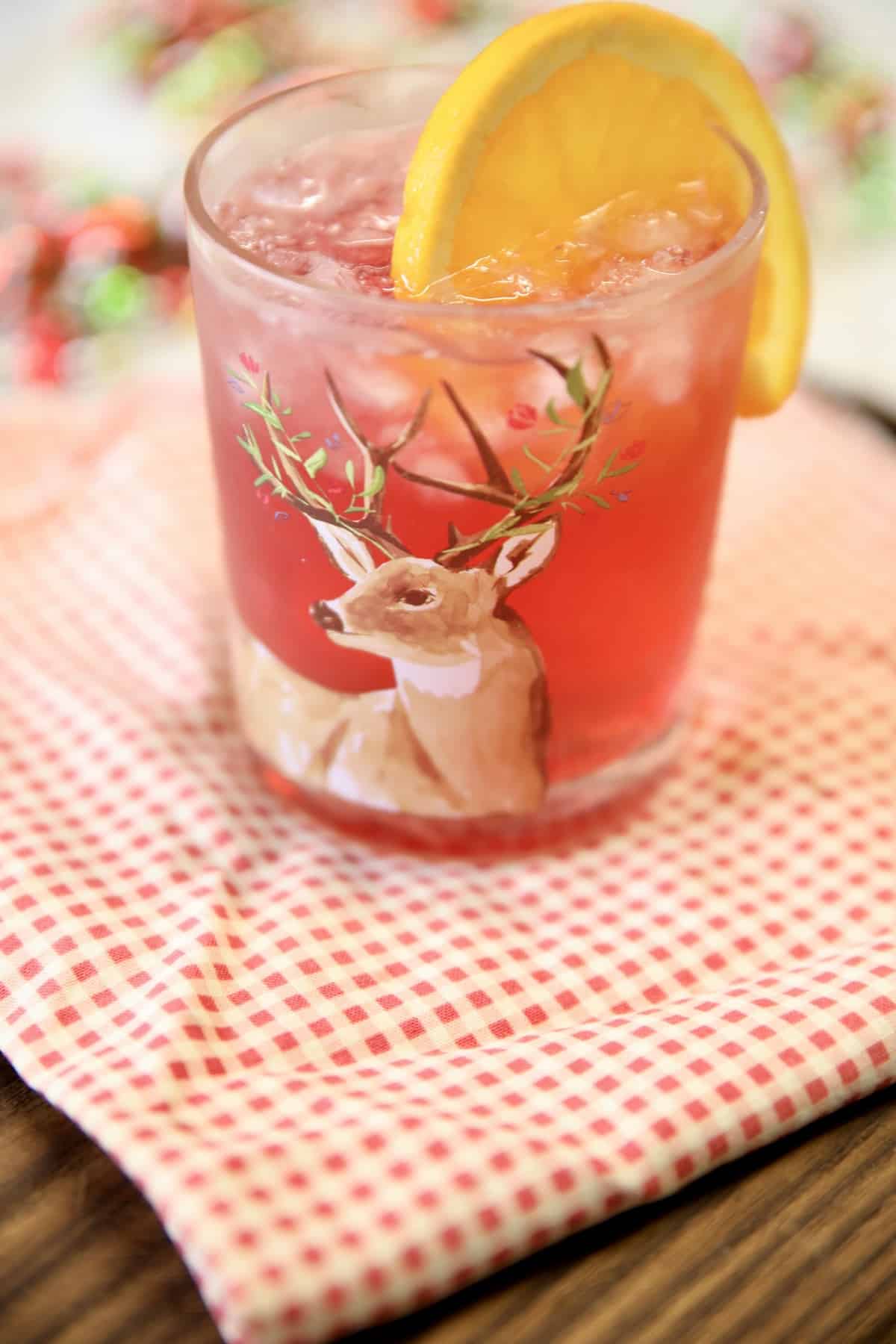 Cranberry cocktail in a glass with orange garnish.