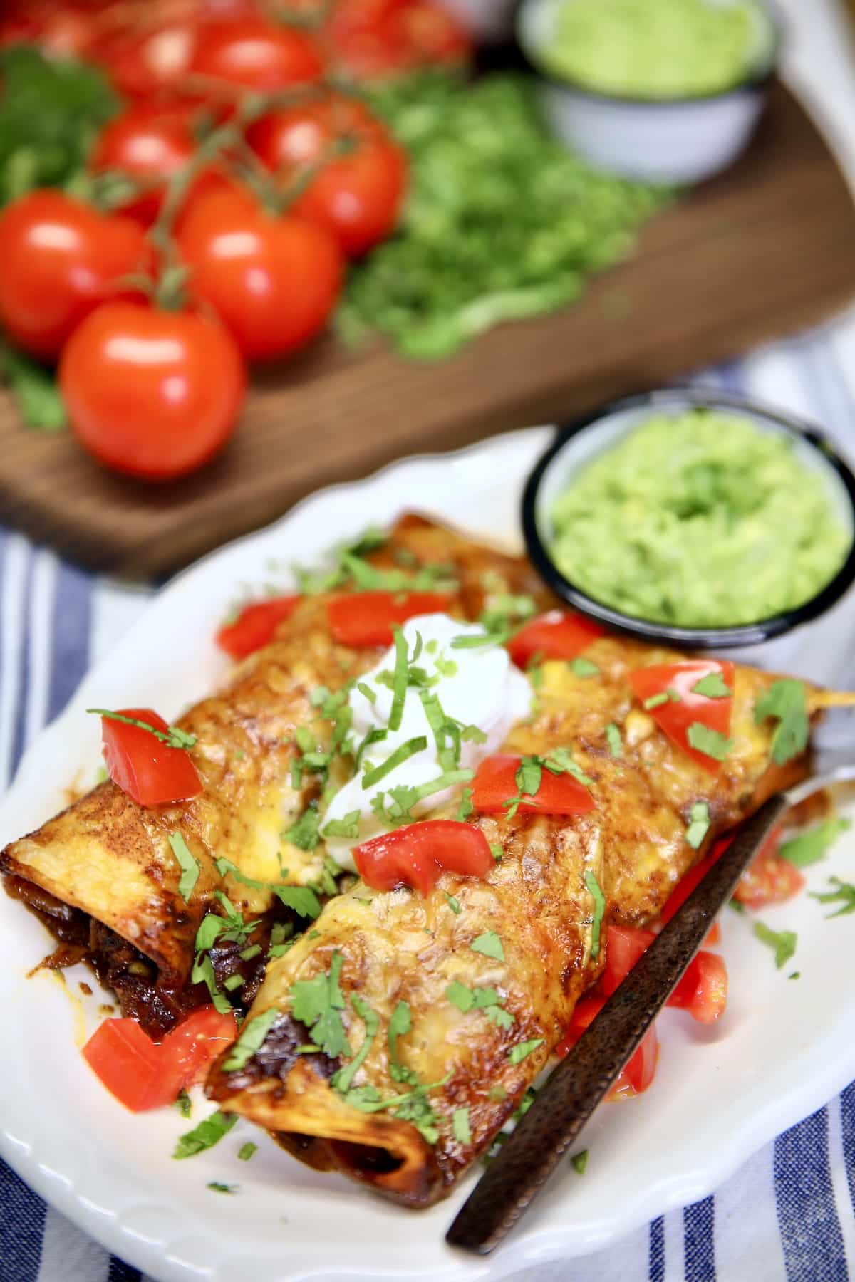 Plate of enchiladas with guacamole, tomatoes, sour cream.