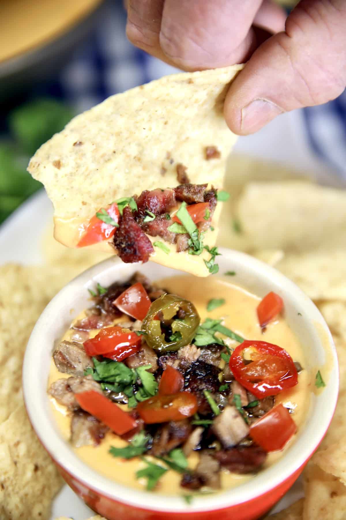 Hand dipping tortilla chip in brisket queso.