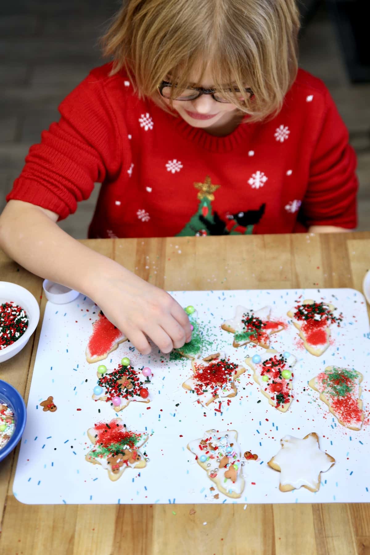 Girl decorating sugar cookies with icing and sprinkles.