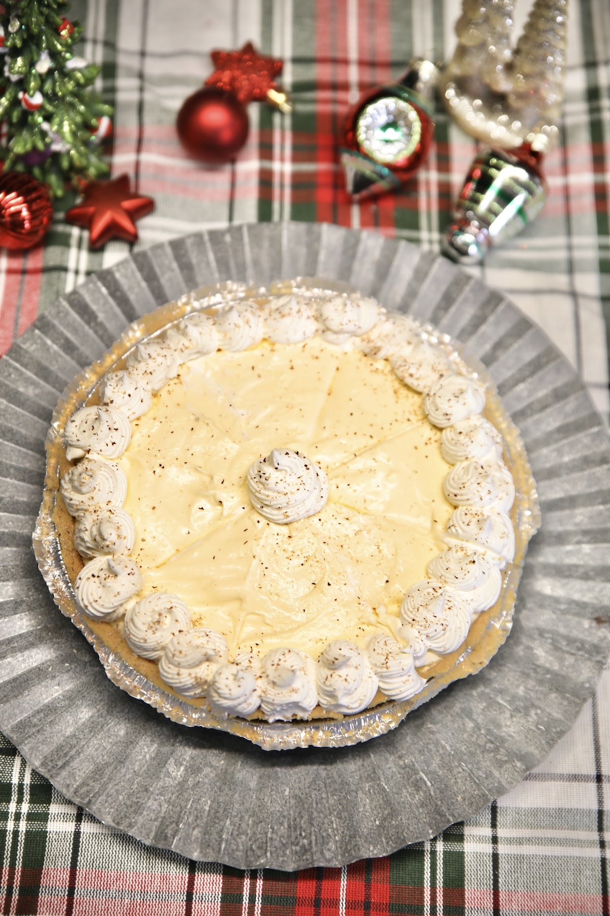 Eggnog cheesecake on a platter, Christmas decor around the platter.