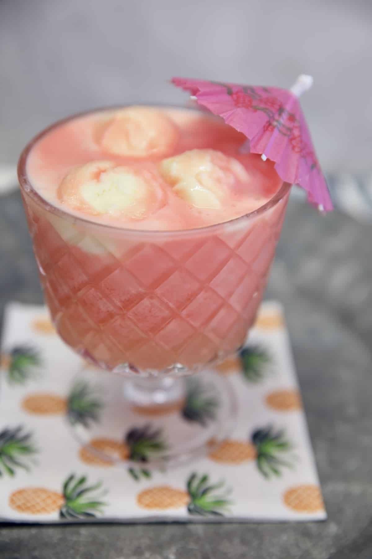 Sherbet punch in a glass with drink umbrella on a pineapple napkin.