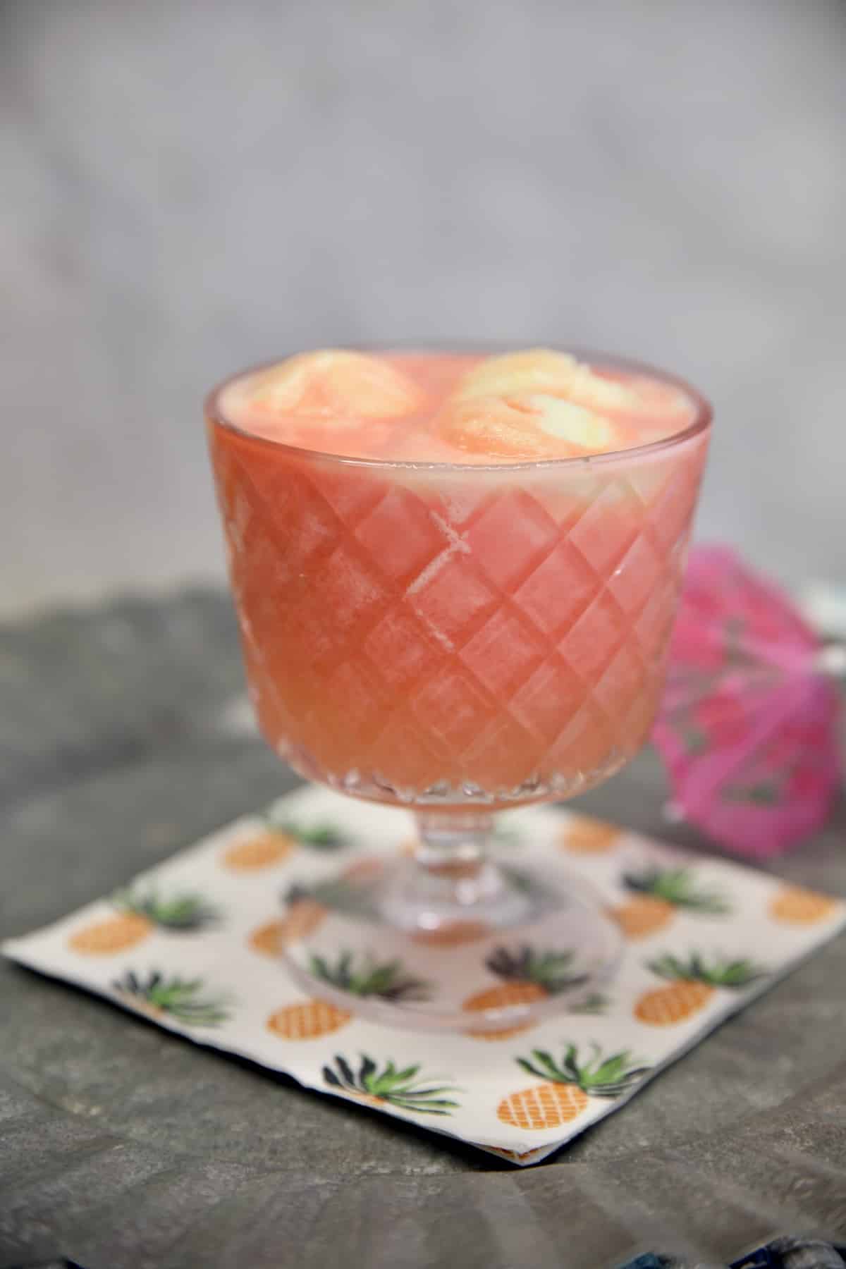Glass with pink sherbet punch on a pineapple print napkin.