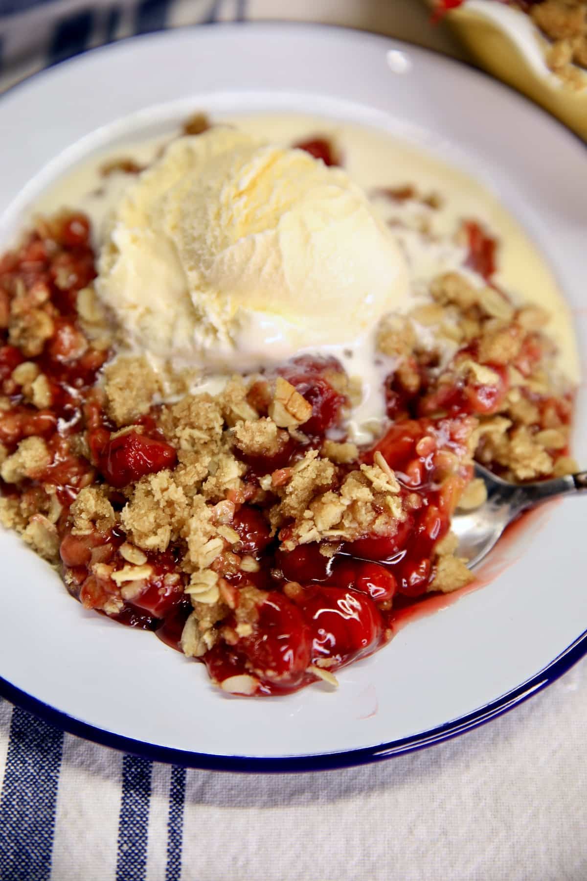 Cherry crisp with vanilla ice cream on a dessert plate.