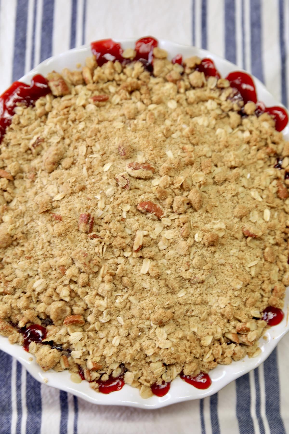 Baked cherry crisp in a pie plate on a striped cloth.