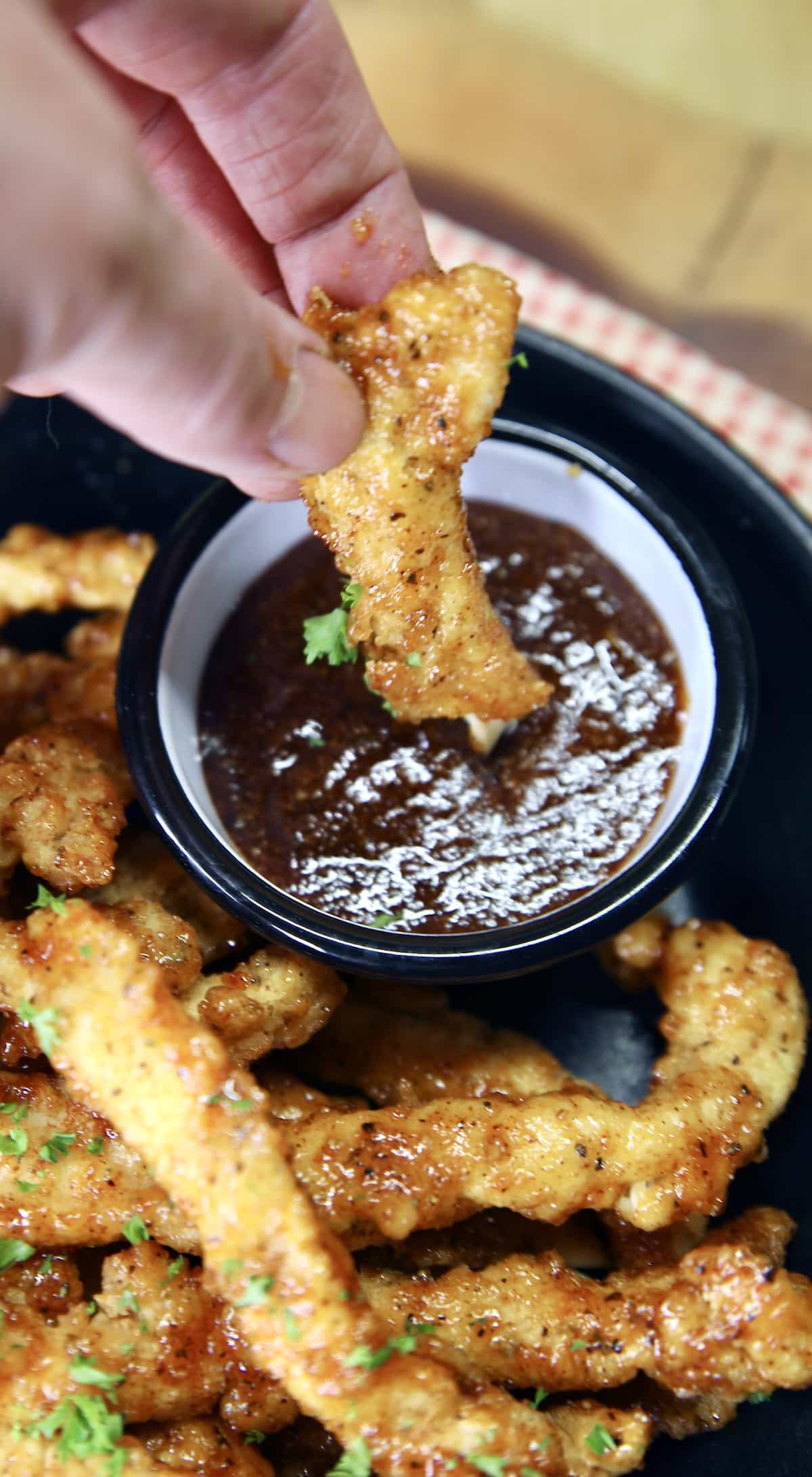 Chicken fries dipping in bbq sauce.