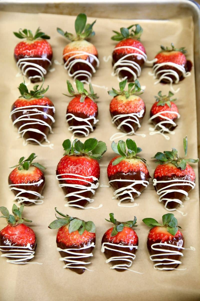 Chocolate covered strawberries with white drizzle on parchment.