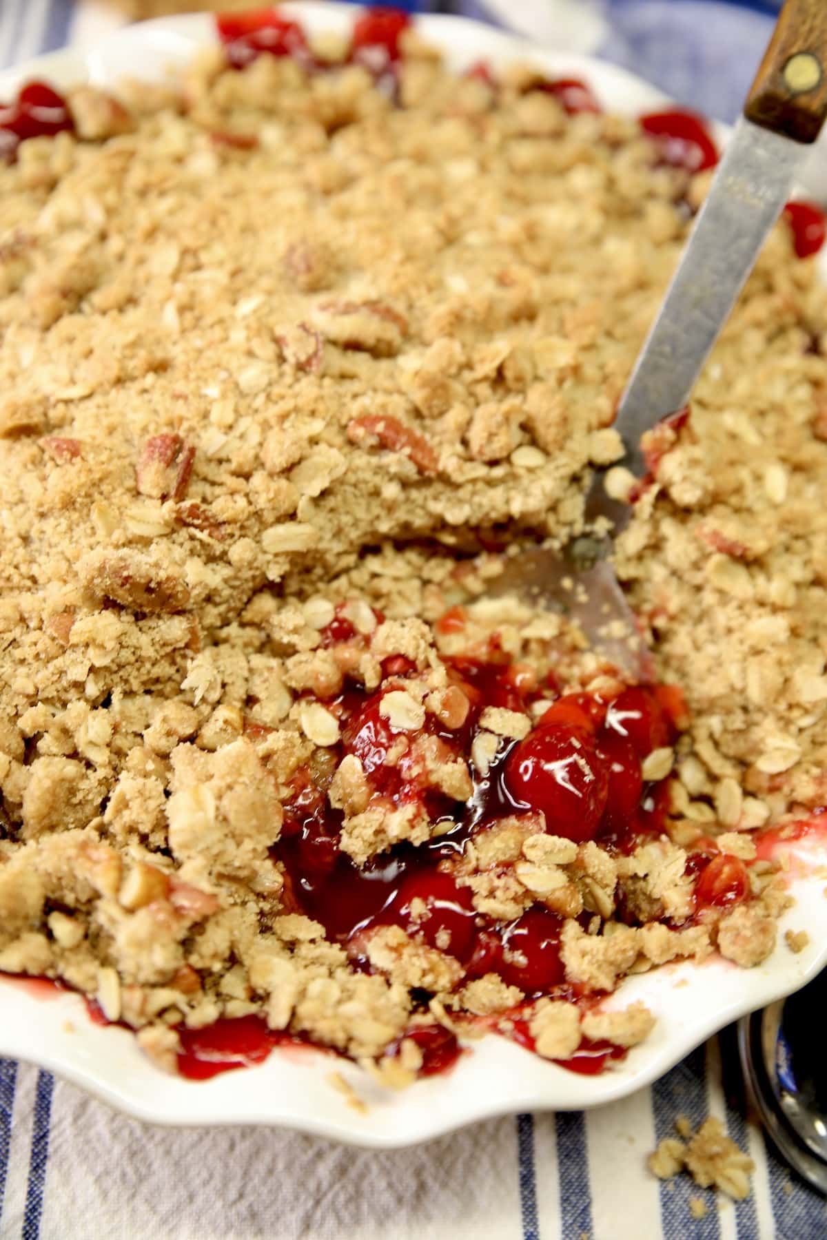 Pie plate of cherry crisp, with spoon scooping.