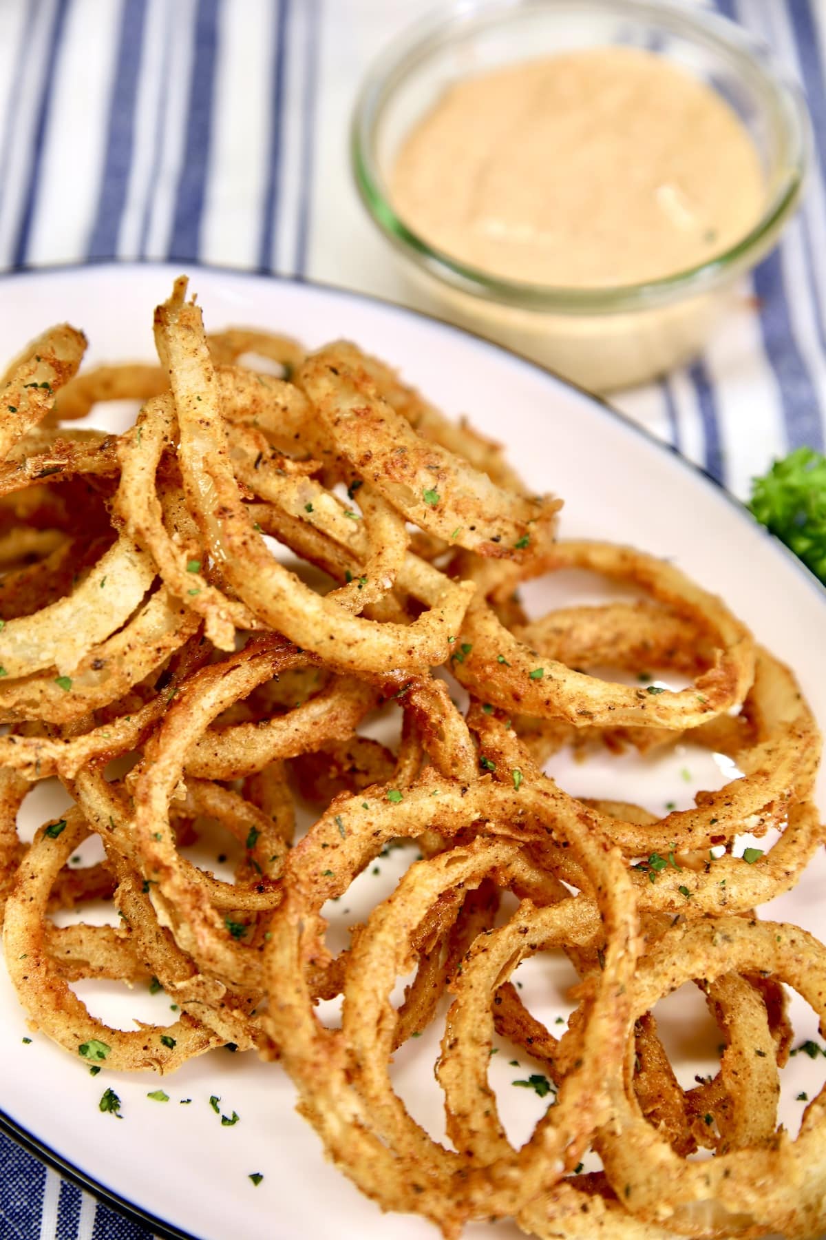 Fried onion rings on a platter with bowl of dipping sauce.