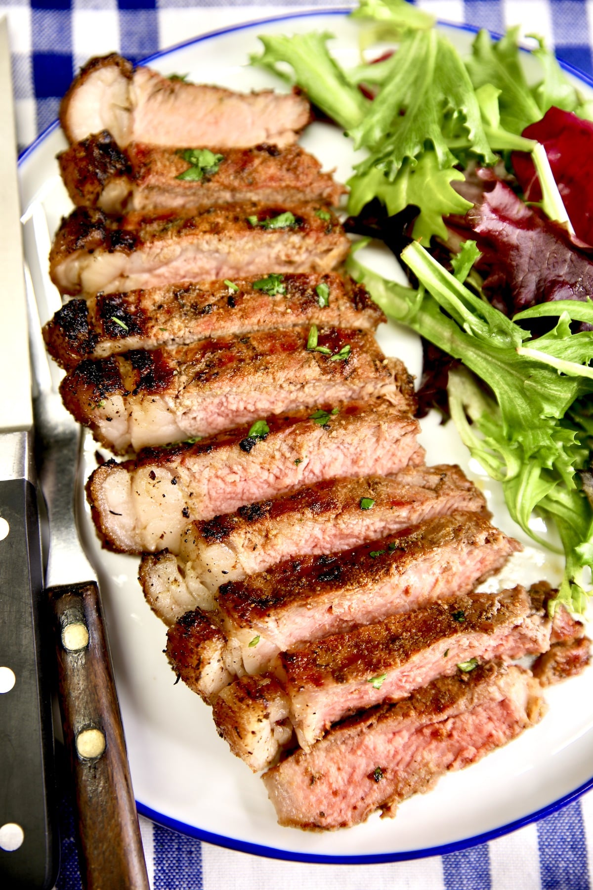 Sliced NY Strip steak on a plate with salad.
