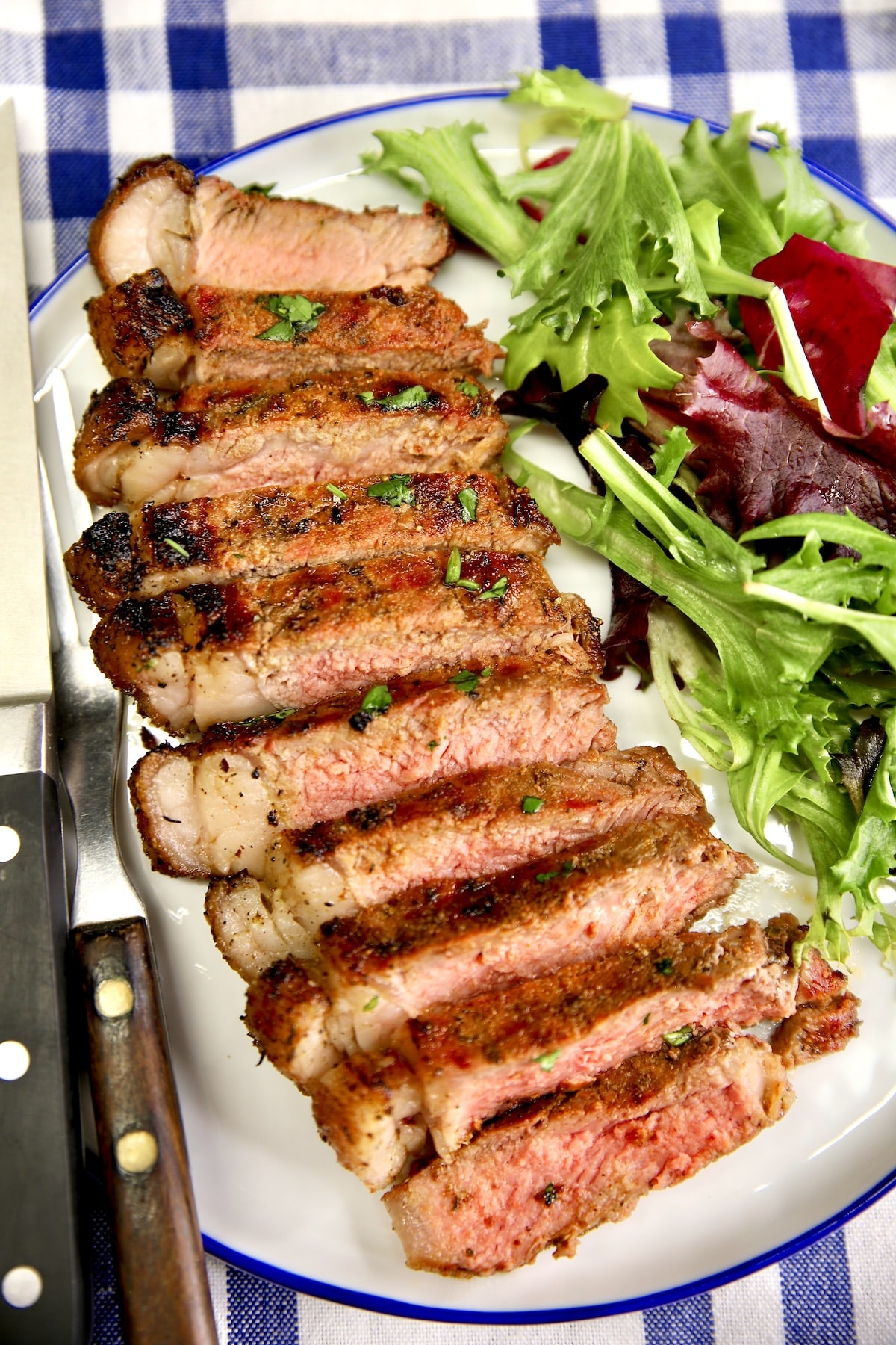 Plate of sliced grilled steak and salad greens.