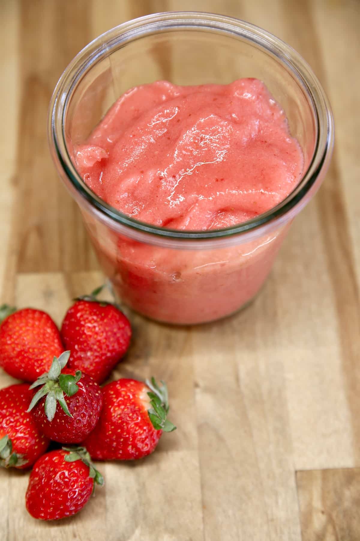 Jar of strawberry puree and fresh strawberries.
