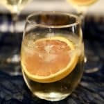 Stemless wine glass with white wine spritzer, orange wheel garnish.
