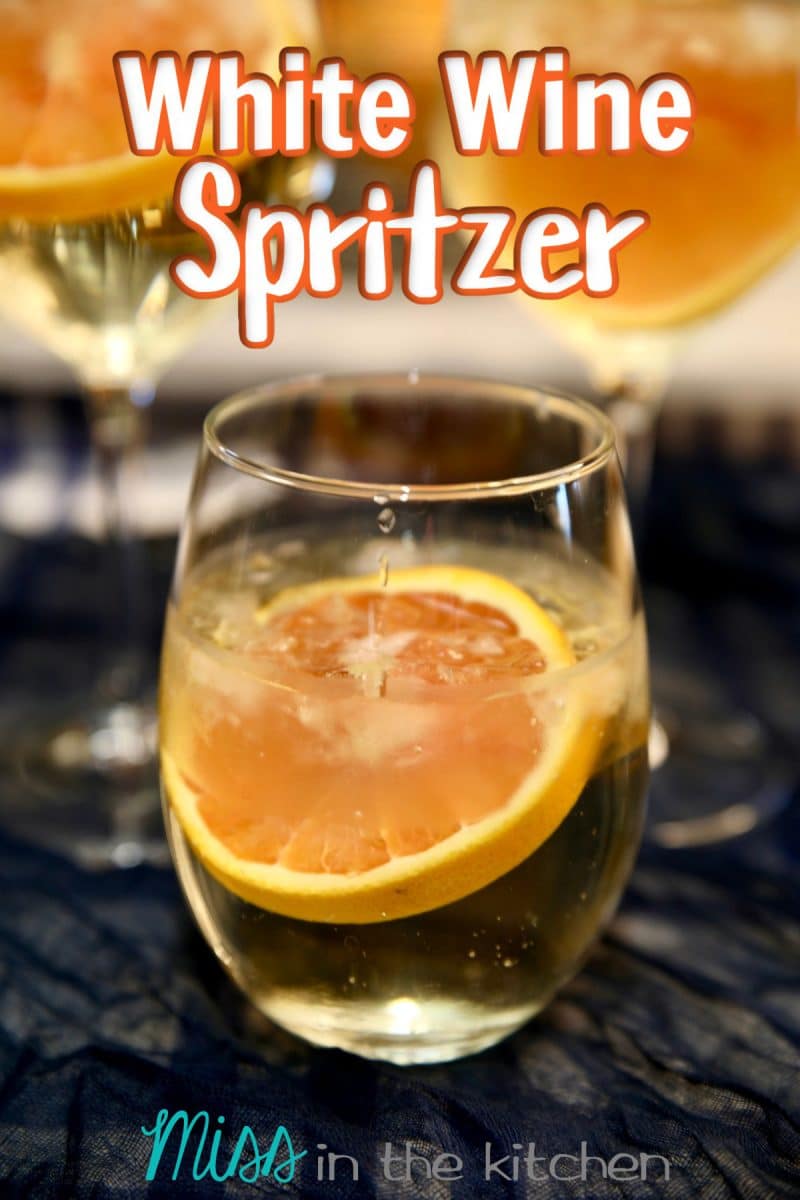 White wine spritzer in a stemless glass with orange wheel. Text overlay.