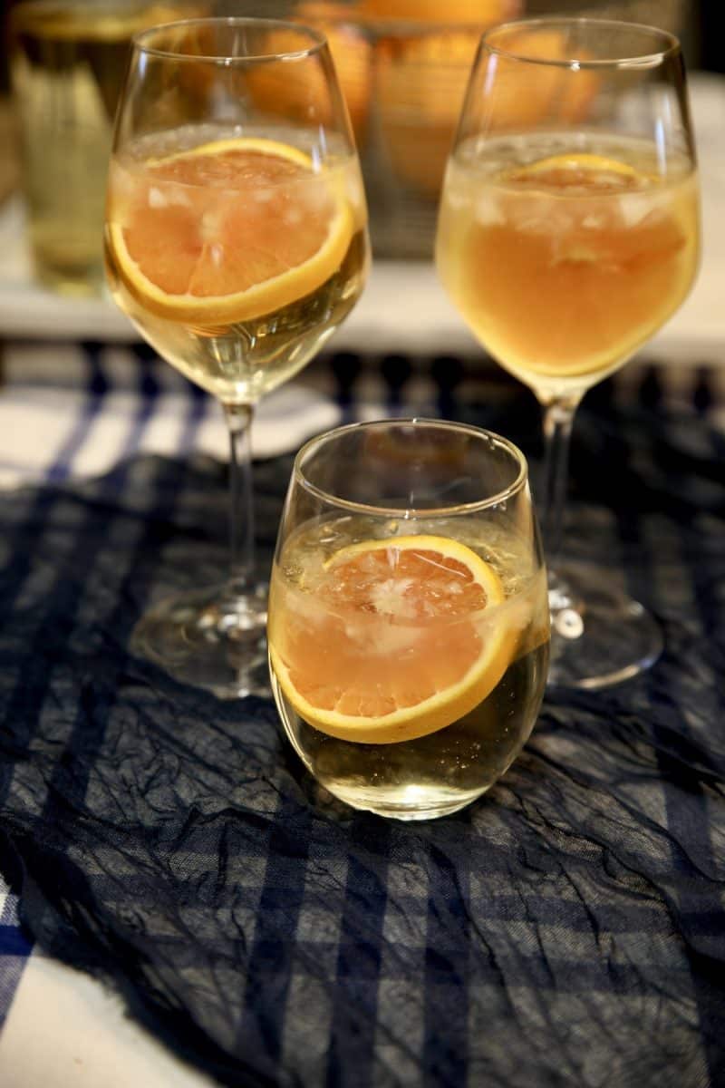 White wine spritzers: 3 glasses, 1 stemless. Orange garnish.