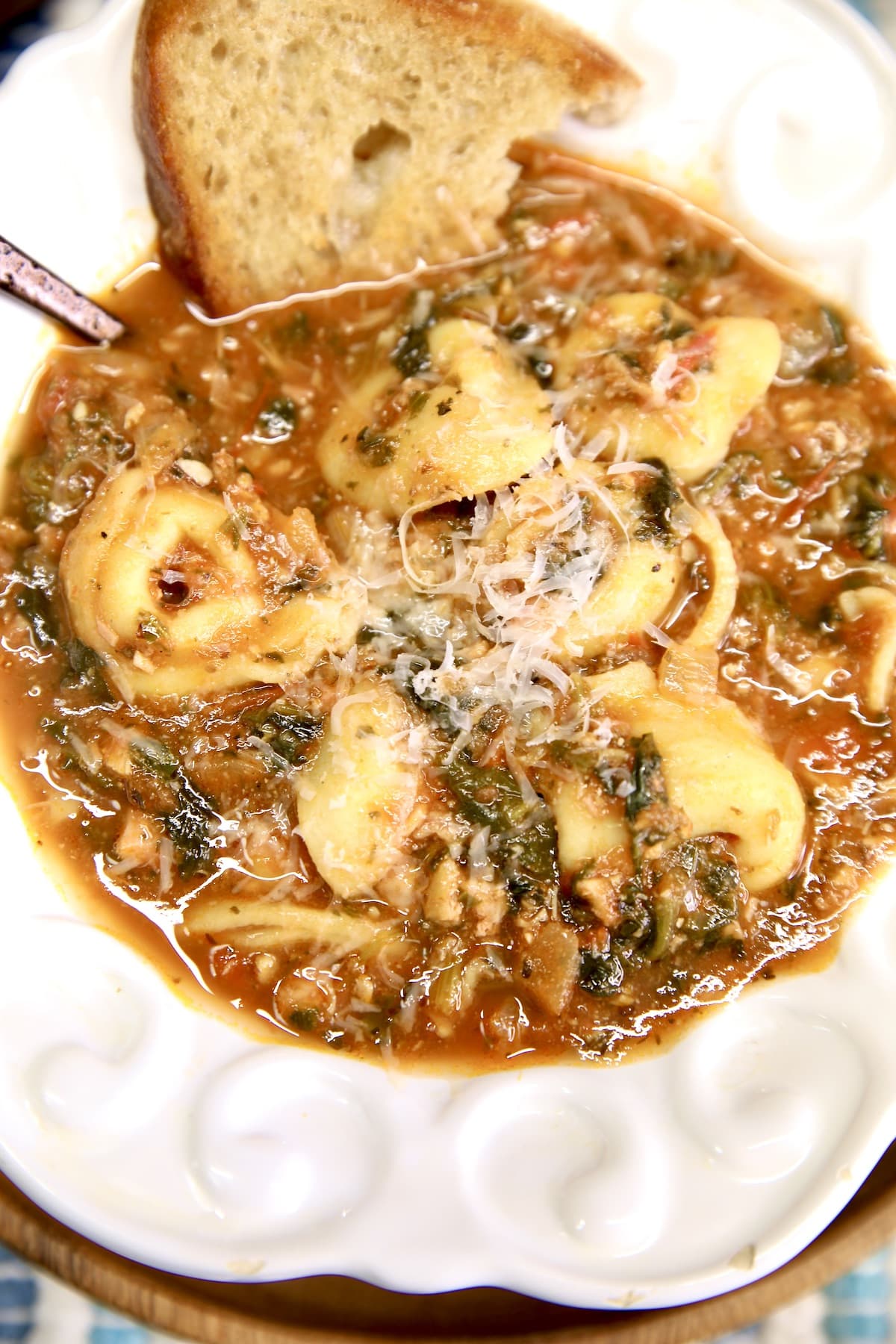 Closeup of bowl of tortellini tomato soup with parmesan cheese and bread.
