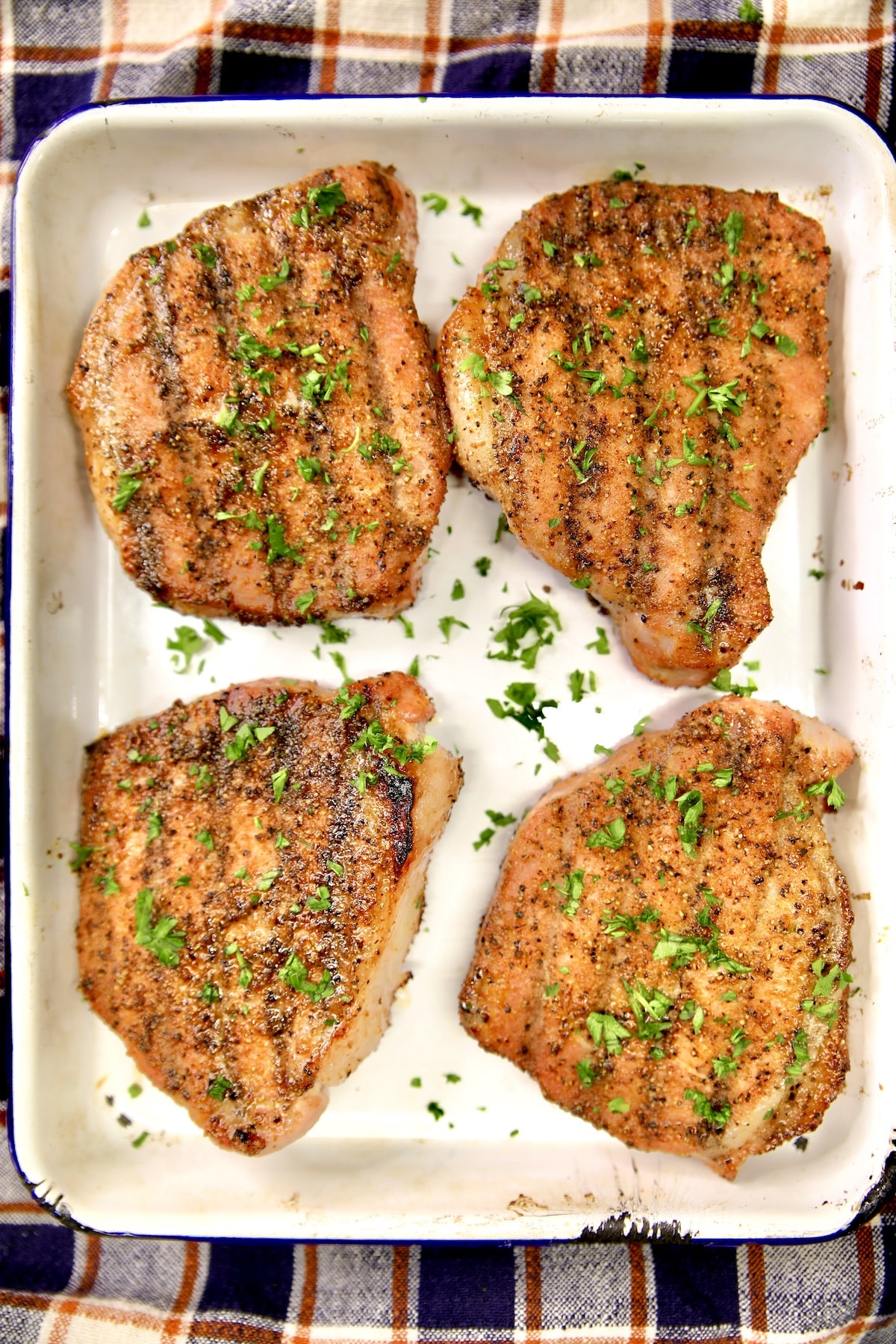4 grilled pork chops on a white tray.