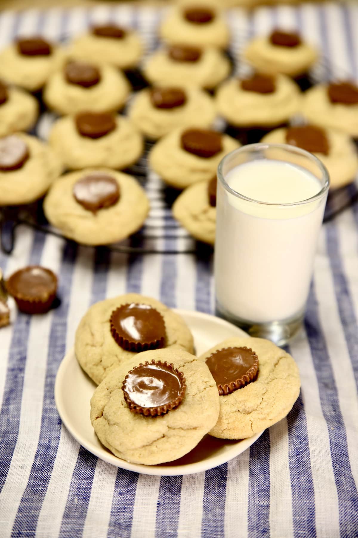 3 peanut butter cup cookies on a plate, cooling rack and glass of milk.