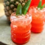 2 glasses red rum punch with fresh pineapple frond garnish.