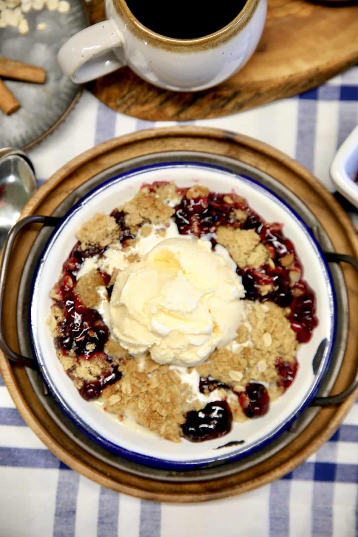 Bowl of blueberry crisp with vanilla ice cream. Cup of coffee.