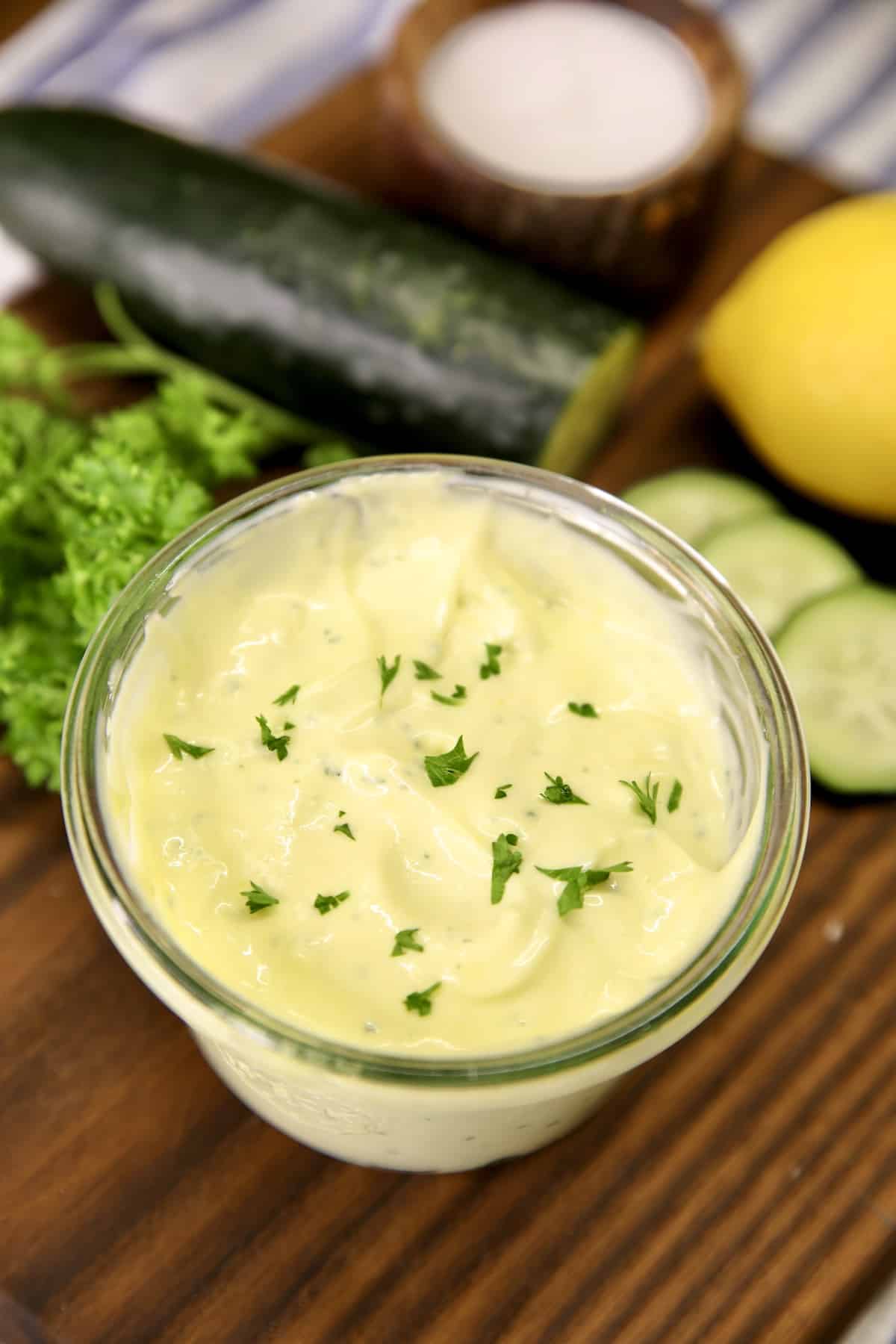 Jar of mayonnaise on a board with cucumbers and lemon.