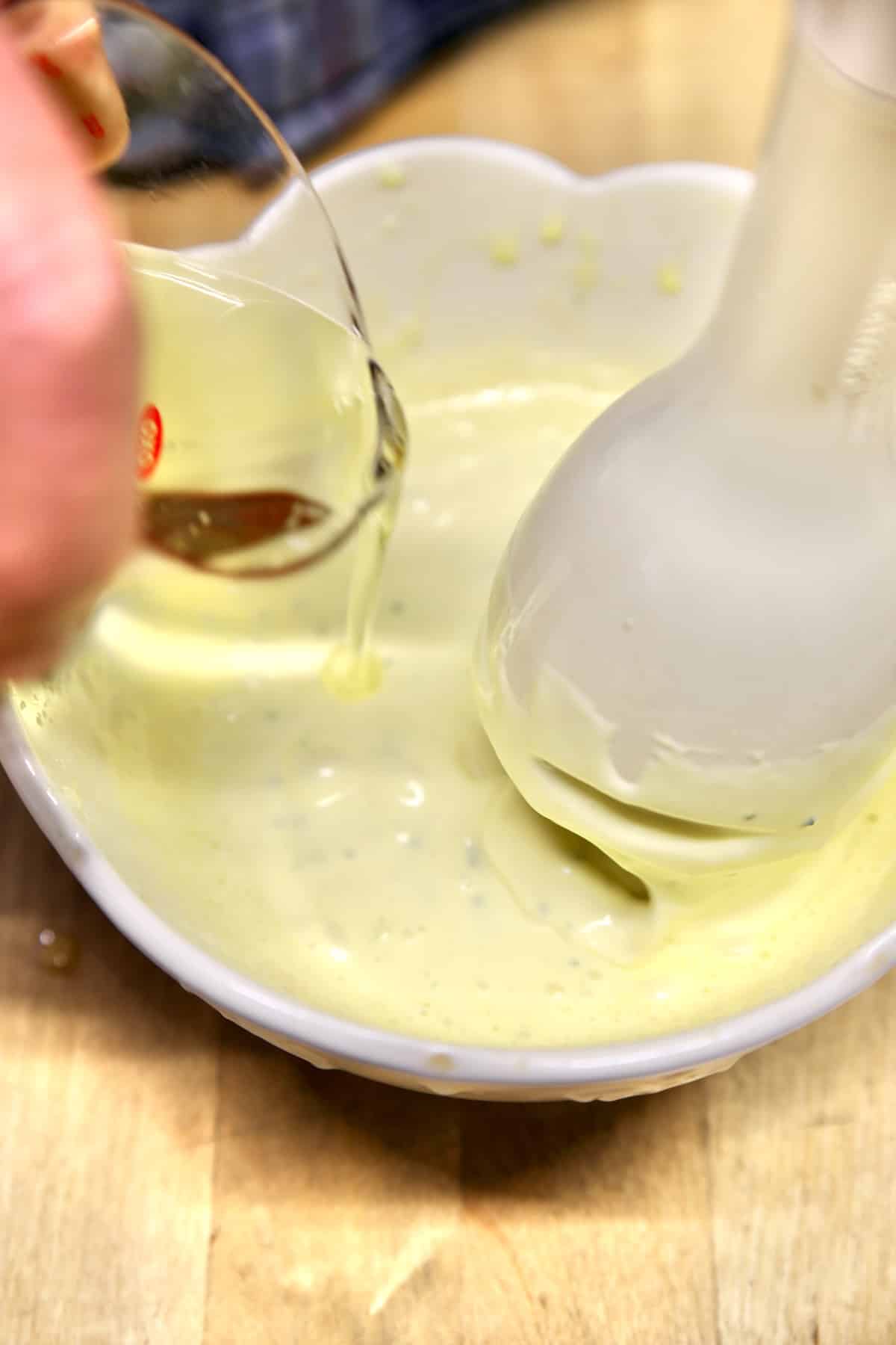 Drizzling oil into bowl making mayo with stick blender.