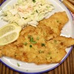 Pork schnitzel on a plate with coleslaw and lemon slice.