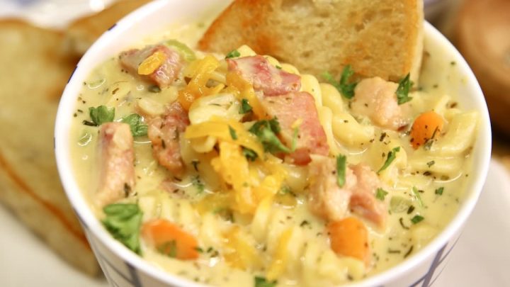 Ham Soup with pasta, vegetables and cheese and a slice of bread in a soup cup.