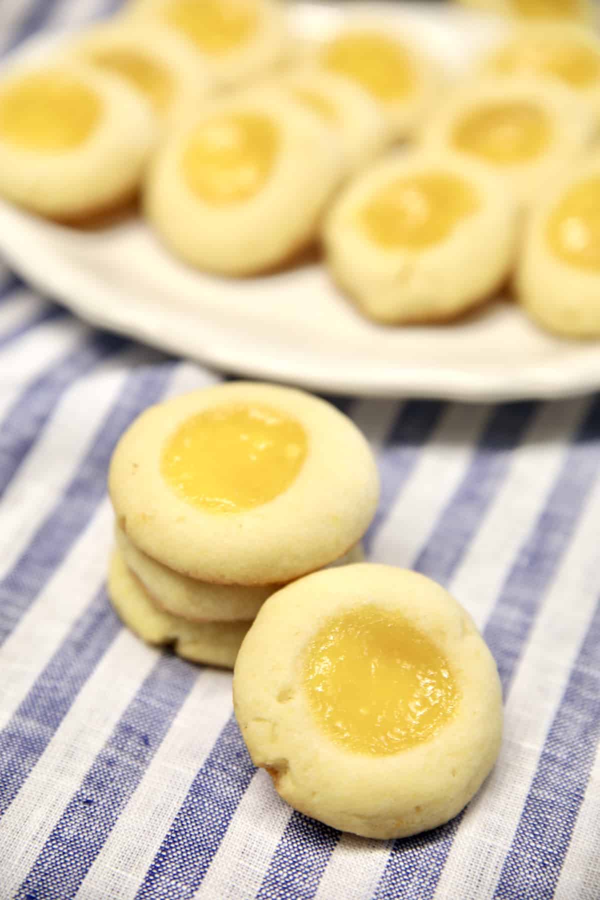 Lemon curd cookies, stacked on a blue and white striped cloth. Platter in background.