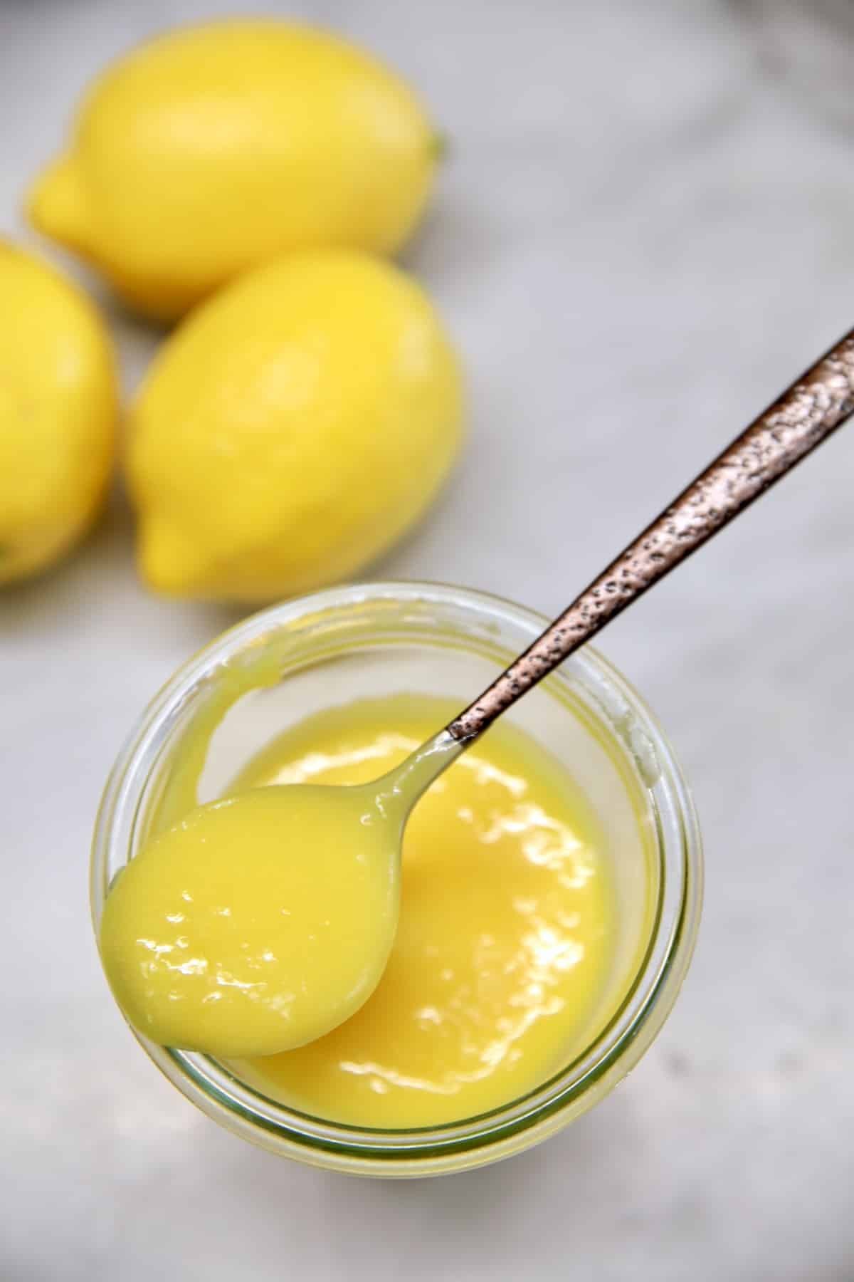 Lemon curd in a jar with spoonful on the top. Whole lemons in background.