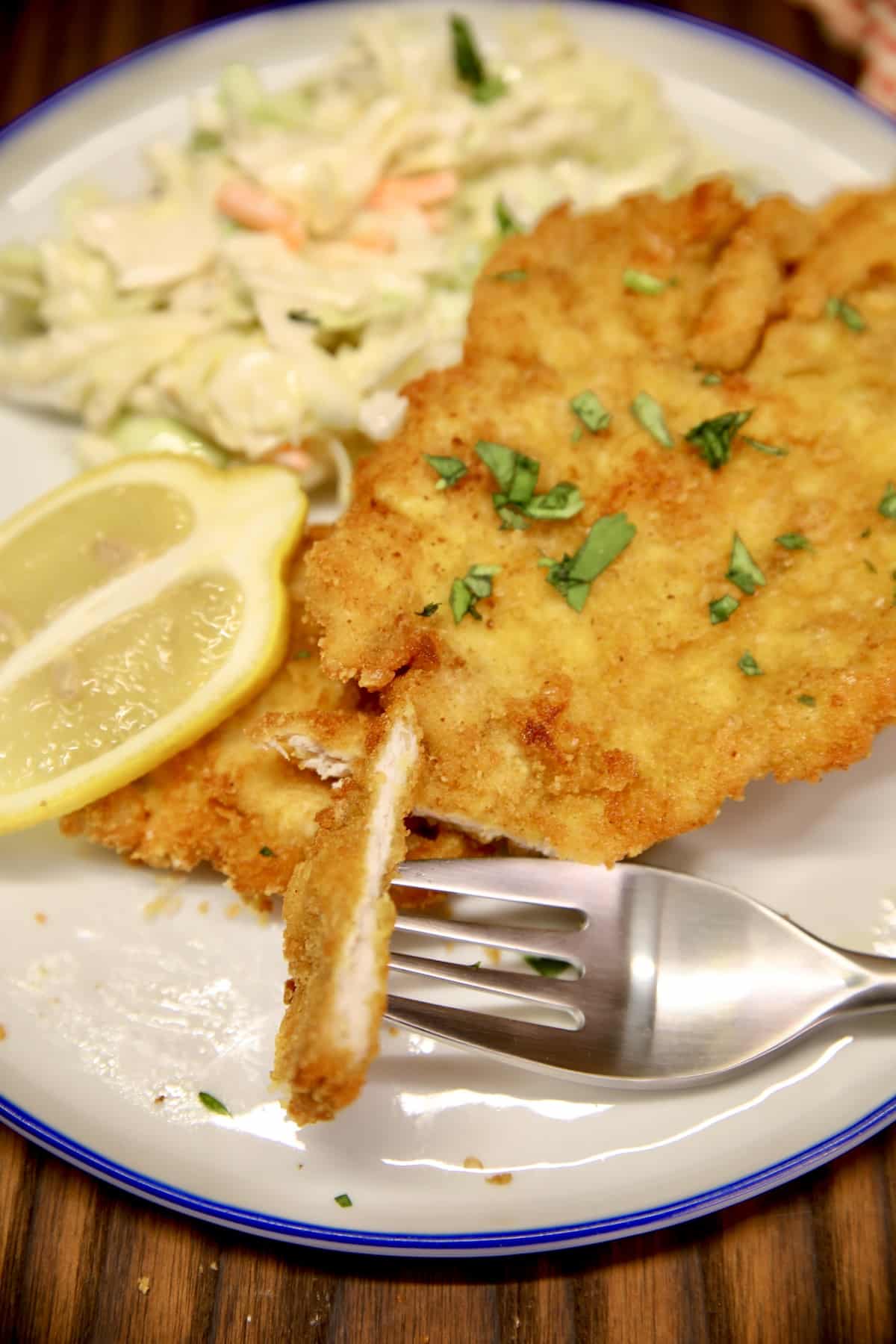 Pork schnitzel on a plate with lemon and coleslaw. Bite on a fork.