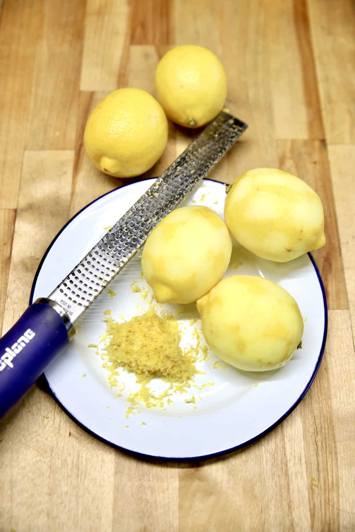 Whole lemons on a plate and cabinet, 3 zested with zester.