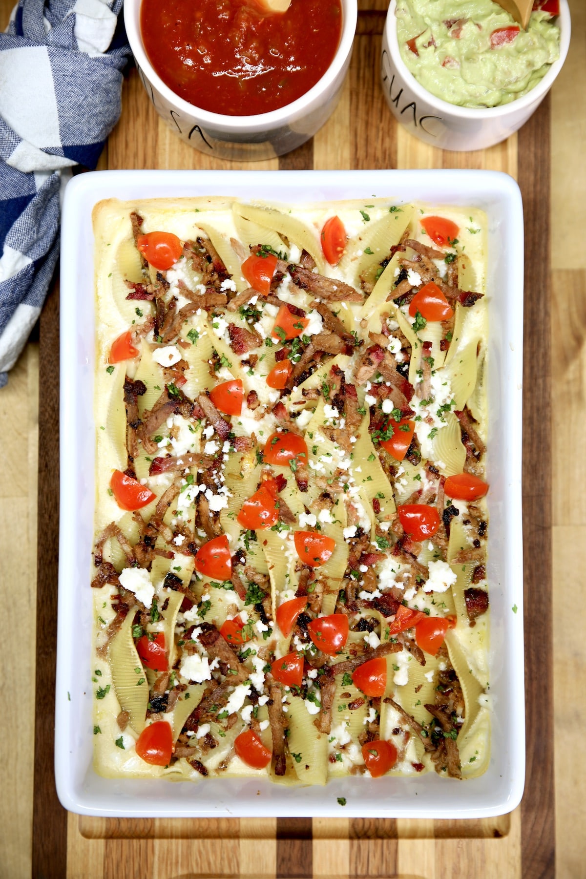 Casserole with brisket stuffed shells, topped with tomatoes, queso fresco cheese.