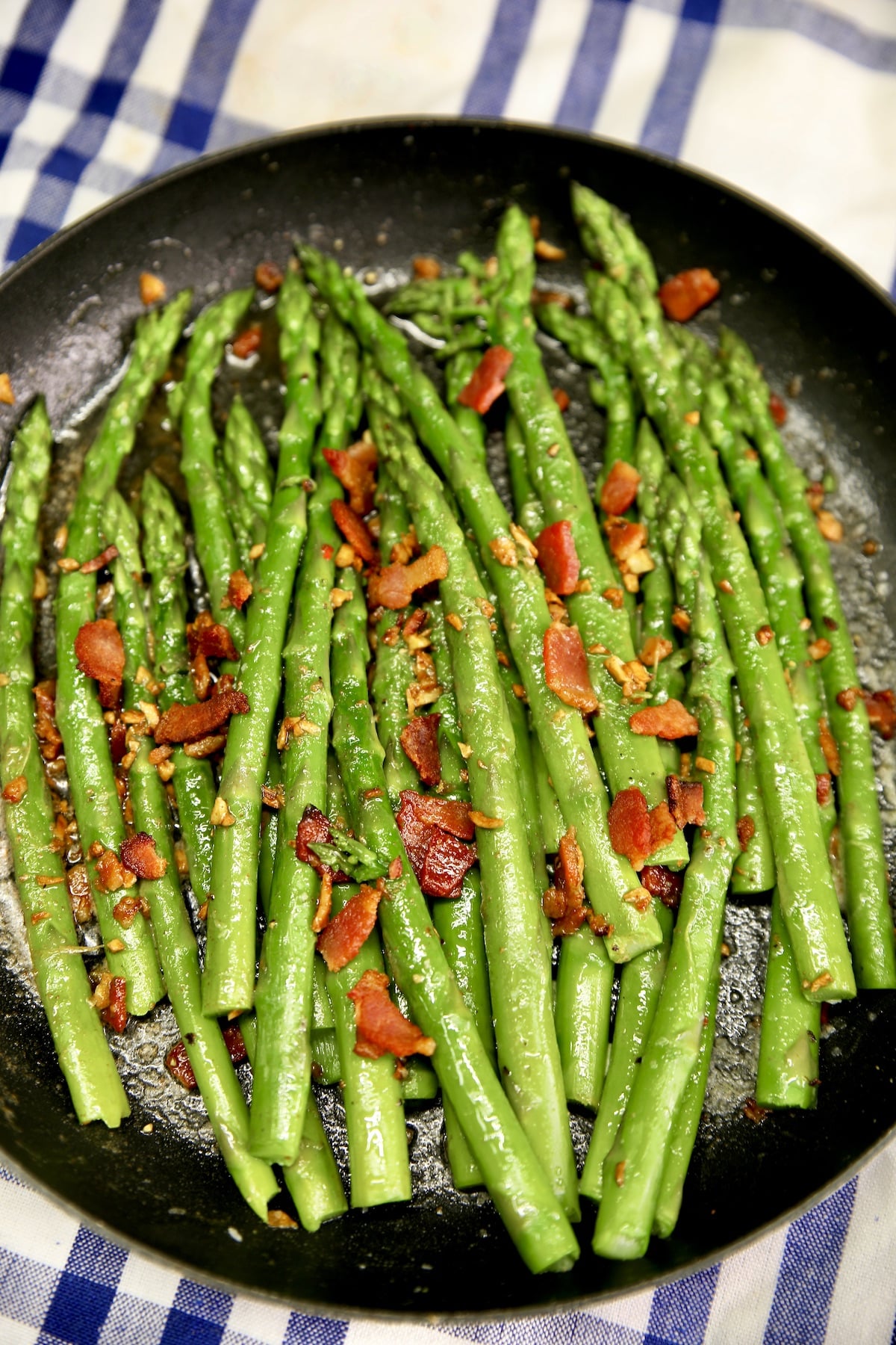 Skillet of asparagus spears topped with garlic butter and bacon crumbles.