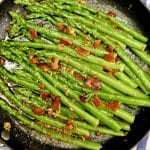 Asparagus in a skillet with garlic and crispy bacon.