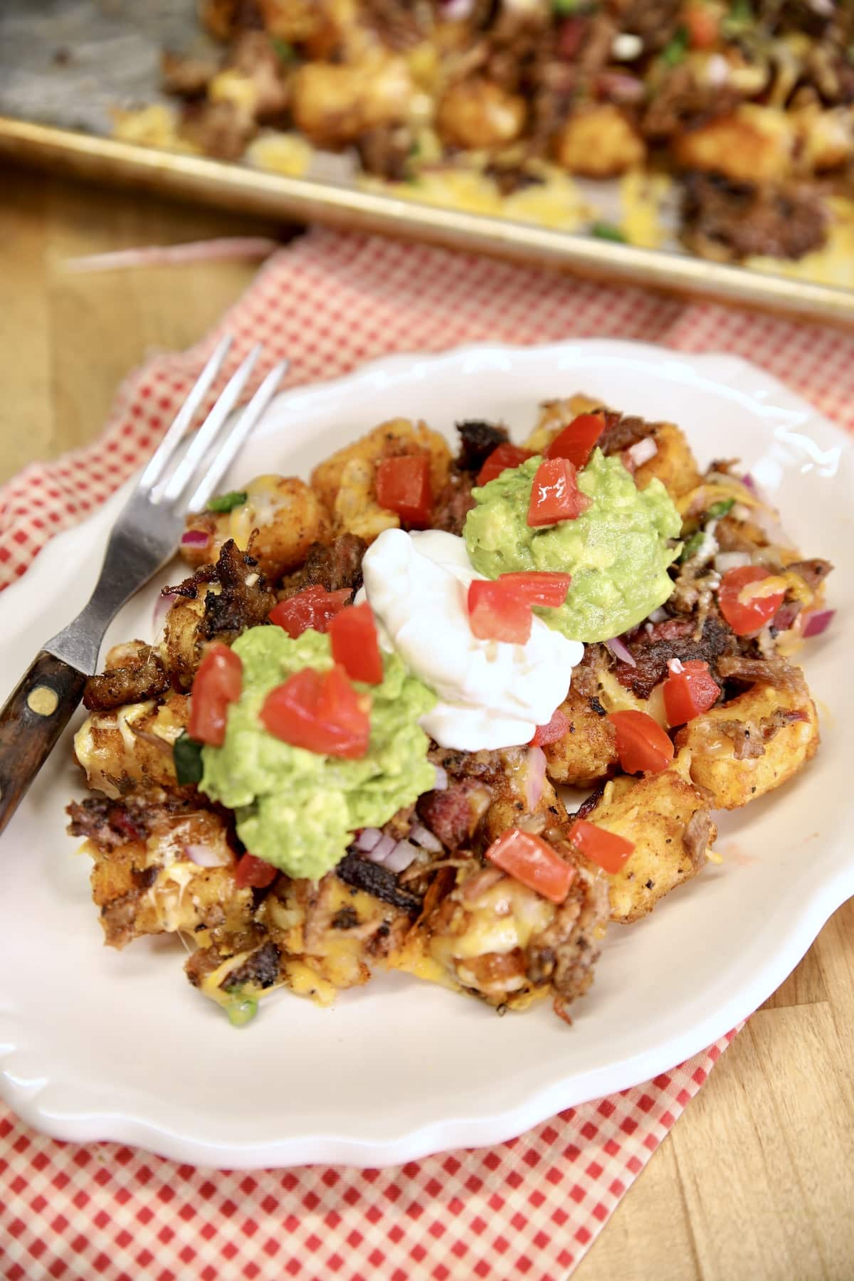 Tater tot nachos on a plate, topped with sour cream and guacamole.