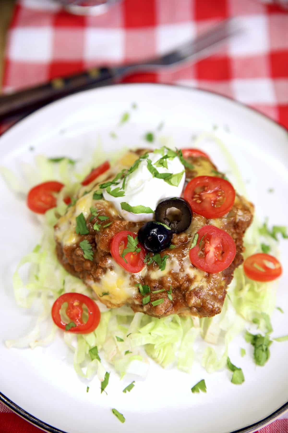 Plate with burrito bake casserole. Topped with sour cream, tomatoes, olives.