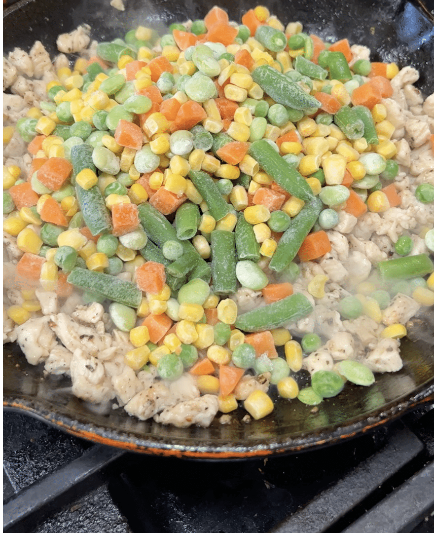 Adding mixed frozen vegetables to chicken in a skillet.
