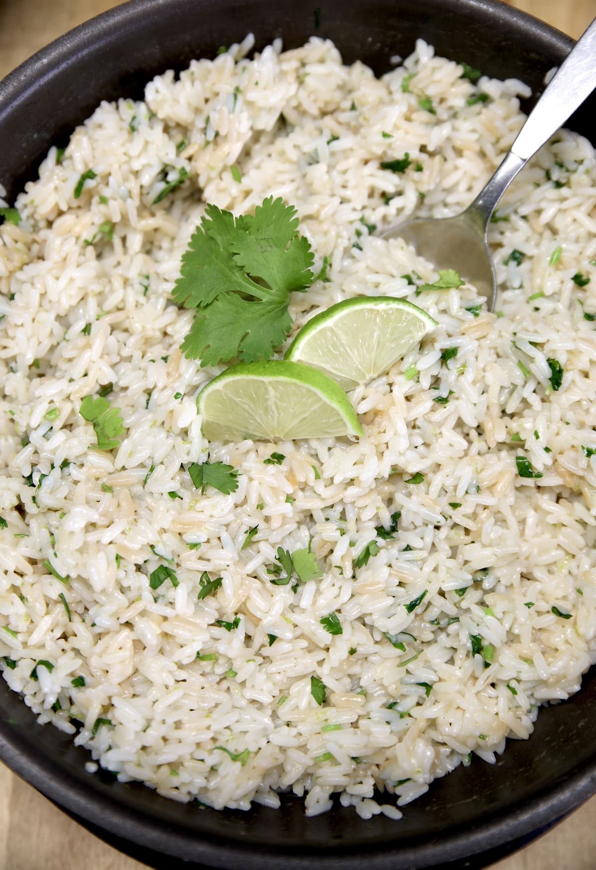 Bowl of cilantro lime rice with a spoon, lime slices, cilantro garnish.