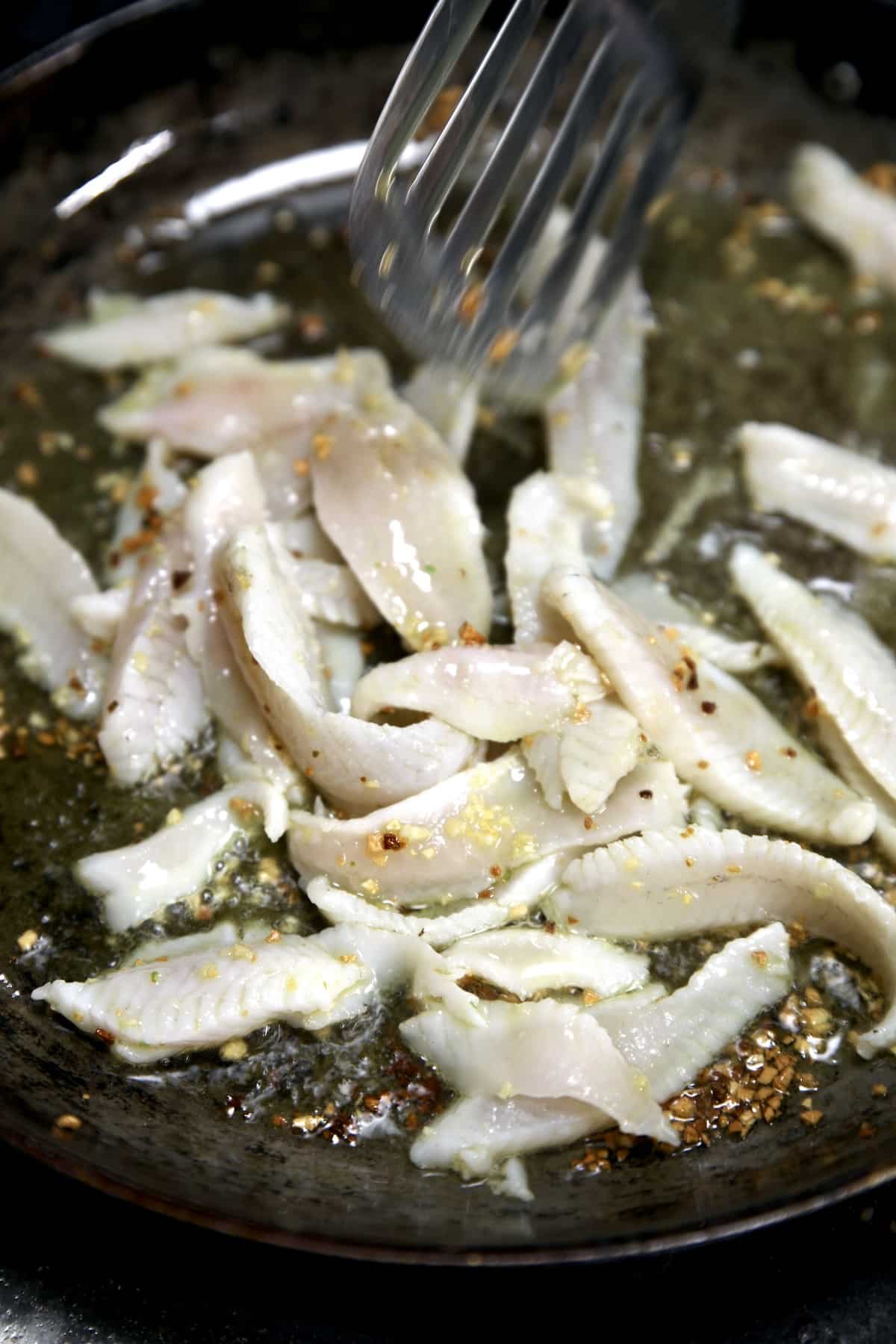 Cooking fish filets in a skillet with garlic and olive oil.