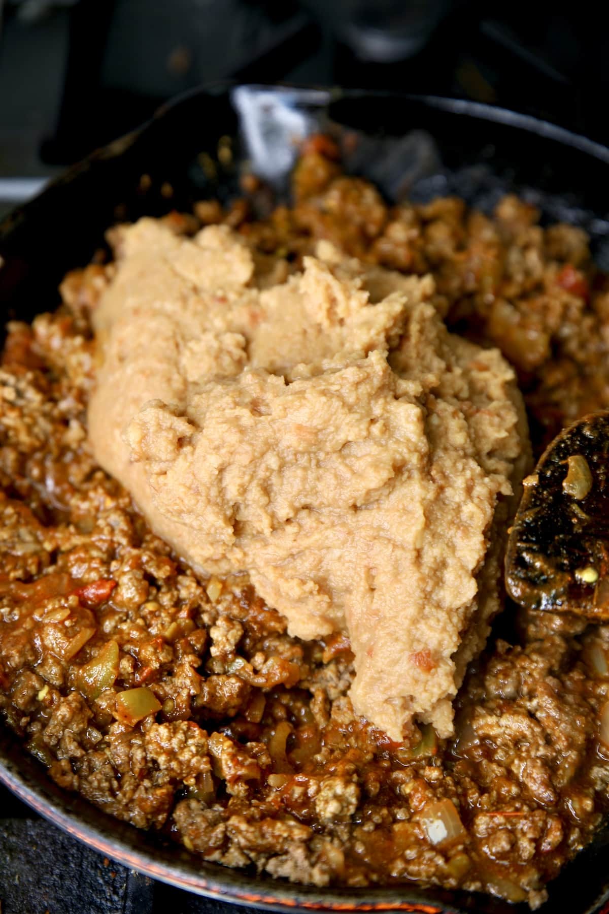 Adding refried beans to skillet with ground beef.