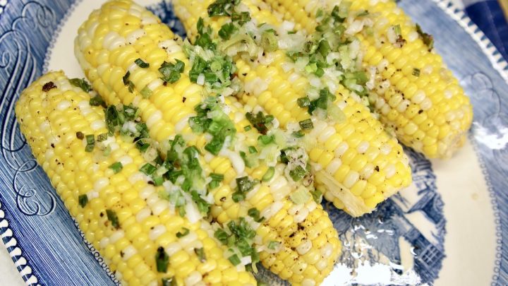 Platter with 4 corn on the cob topped with green onions.